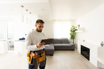 repair, construction and building concept - happy smiling worker or builder with tablet pc computer and tools over home room background.