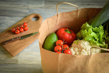 Groceries Shopping Concept. Closeup Reusable Paper Bag With Many Vegetables Fruit Indoors. Cutting Board With Kitchen Knife Cherry Tomatoes On Background. Preparing Food. Ordering Product To Home.