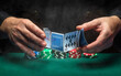 Close-up of the hands of a dealer or croupier shuffling poker cards in a smoky club against a green table with chips. Concept of playing poker or gaming business