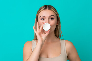 Wall Mural - Young caucasian woman isolated on blue background with moisturizer