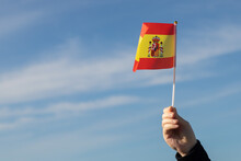 Spanish Flag In Hand Flutters In The Wind Against The Sky