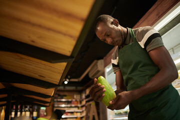 Wall Mural - Supermarket worker putting green mangoes on shelf