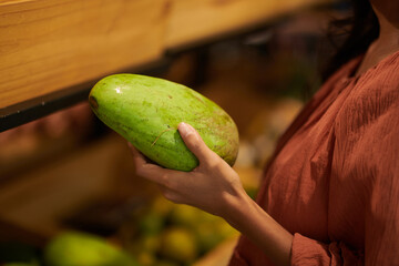 Wall Mural - Closeup image of woman buying green mangoes in in grocery store