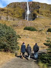 Wall Mural - A group of people 2 women and man walking towards an iconic waterfall in iceland. Tourism in icleand