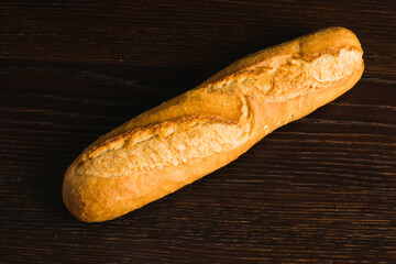 Appetizing french baguette with crust on dark wooden table, background with space for text