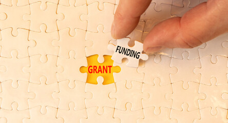 Grant funding symbol. Concept words Grant funding on white paper puzzles. Beautiful yellow table white background. Businessman hand. Business and grant funding concept. Copy space.
