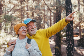 Head shot portrait close up of middle age cheerful people smiling and looking at the the trees of the forest around them. Active couple of old seniors hiking and walking together in the mountain 