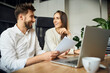 © baranq - Shot of two happy coworkers in small business office discussing. Casual businessman and businesswoman talking sitting at desk