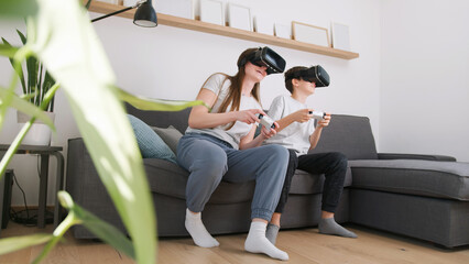 Caucasian girl and her young brother having fun at home, playing driving simulation video games by using virtual reality headsets and controllers