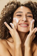 Woman beauty face close-up applying foam to wash and cleanse skin with fingers of her hand, nail and hair health, hair dryer style curly afro hair, body and beauty care concept