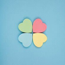 Collection Of Different Heart Pastel-colored Sheets Of Note Papers Ready For Your Message In Shape Of Four-leaf Clover On Blue Background. Top View. Close Up. Sticky Notes.