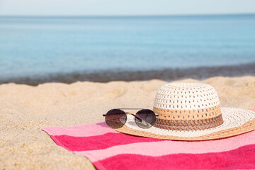 Wall Mural - Beach towel with straw hat and sunglasses on sand near sea. Space for text