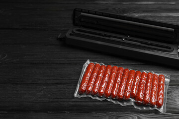 Wall Mural - Vacuum packing sealer and plastic bag of sausages on black wooden table, space for text