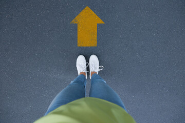 Wall Mural - Planning future. Woman standing in front of drawn mark on road, closeup. Yellow arrow showing direction of way