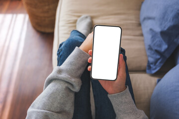 Poster - Top view mockup image of a woman holding mobile phone with blank desktop white screen while lying on a sofa at home