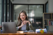 © Songsak C - The cheerful business lady working on a laptop in the office, an Asian happy beautiful businesswoman in a formal suit working in the workplace. Attractive female employee office worker smile.