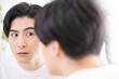 鏡で髪の毛や肌をチェックするアジア系の男性