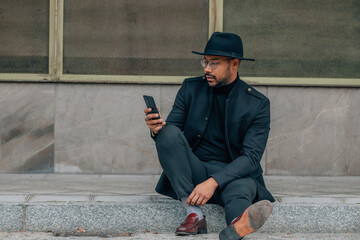 Wall Mural - businessman with mobile phone in the street sitting on the sidewalk