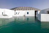 Fototapeta Sawanna - Exterior of the modern building of Louvre in Abu Dhabi, with the latticework dome and the white marble wall, surrounded by water