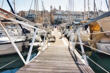 Point-of-view Shot From The Entrance Of A Wooden Jetty Pier Leading To Expensive Harbored Yachts In A Marina