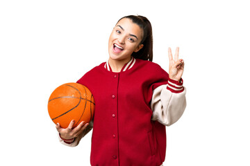 Wall Mural - Young Woman playing basketball over isolated chroma key background smiling and showing victory sign