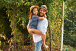 © _KUBE_ - Family's vacation. Happy bearded father in a straw hat hugs his daughter. Garden in the background. The concept of Father's Day and happy childhood