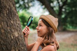© _KUBE_ - Children's education. Portrait of amazement little girl in a straw hat looks at the tree bark through a magnifying glass. The concept of scouting and curious childhood