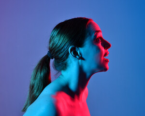 Wall Mural - Head and shoulders close up portrait of pretty girl with expressive facial expressions, with  colourful neon gel lighting, isolated on studio background.