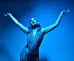 Wall Mural - close up portrait of pretty girl with blue hair wig and elegant gown, with expressive facial expressions and gestural arm poseswith  colourful neon gel lighting, isolated on studio background.