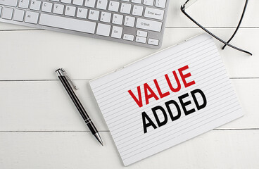 Poster - VALUE ADDED text on notebook with keyboard , pen glasses on white wooden background