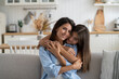 © DimaBerlin - Positive close-knit family of woman and teenager girl snuggle up to each other in living room of apartment. Cheerful smiling mother and daughter hugging looking at camera feeling affection and love