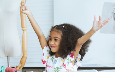 Cute African little girl drawing or sketching clothing design on paper at tailor room, cozy home as her career dream, smiling with happiness and fun. Leisure, Lifestyle, Education, Kid Concept.