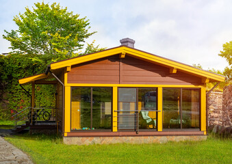 Wall Mural - House with panoramic windows. One-story cottage with lawn. Wooden house in summer weather. Residential cottage with bicycle on terrace. Hedge behind country house. Scandinavian style cottage