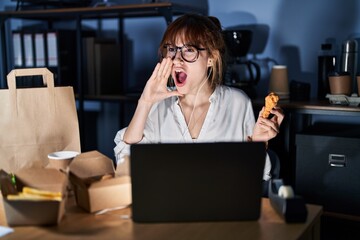 Poster - Young beautiful woman working using computer laptop and eating delivery food shouting and screaming loud to side with hand on mouth. communication concept.