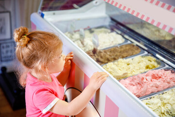 Wall Mural - Cute little toddler girl choosing and buying ice cream in a cafe. Happy baby child looking at different sorts of icecream. Sweet home made dessert