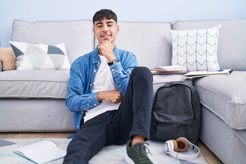 Sticker - Young hispanic man sitting on the floor studying for university with hand on chin thinking about question, pensive expression. smiling and thoughtful face. doubt concept.