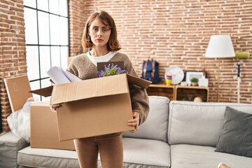 Poster - Young beautiful woman holding box moving to a new home relaxed with serious expression on face. simple and natural looking at the camera.