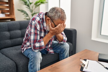 Wall Mural - Senior grey-haired man patient stressed with hands on face sitting on sofa at psychology clinic