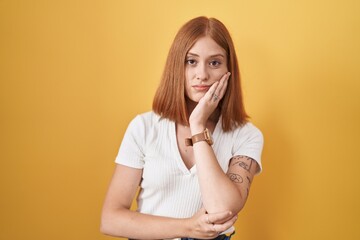 Wall Mural - Young redhead woman standing over yellow background thinking looking tired and bored with depression problems with crossed arms.