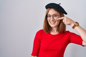 Wall Mural - Young redhead woman standing wearing glasses and beret pointing with hand finger to face and nose, smiling cheerful. beauty concept