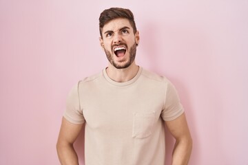 Poster - Hispanic man with beard standing over pink background angry and mad screaming frustrated and furious, shouting with anger. rage and aggressive concept.