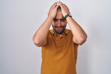 Wall Mural - Hispanic man with beard standing over white background suffering from headache desperate and stressed because pain and migraine. hands on head.