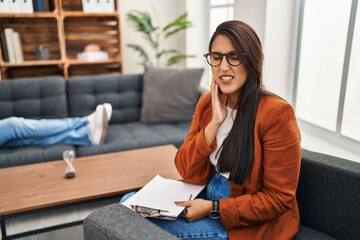 Wall Mural - Young hispanic woman working as psychology counselor touching mouth with hand with painful expression because of toothache or dental illness on teeth. dentist concept.