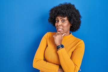 Poster - Black woman with curly hair standing over blue background thinking worried about a question, concerned and nervous with hand on chin