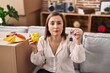 © Krakenimages.com - Middle age hispanic woman holding piggy bank at new home relaxed with serious expression on face. simple and natural looking at the camera.