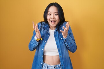 Poster - Young asian woman standing over yellow background celebrating crazy and amazed for success with arms raised and open eyes screaming excited. winner concept