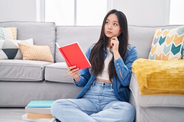 Sticker - Young chinese woman reading book with doubt expression at home