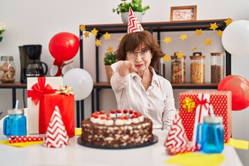 Wall Mural - Middle age woman celebrating birthday holding big chocolate cake pointing with finger to the camera and to you, confident gesture looking serious