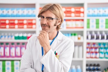 Canvas Print - Caucasian man with mustache working at pharmacy drugstore looking confident at the camera smiling with crossed arms and hand raised on chin. thinking positive.