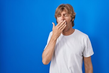 Poster - Middle age man standing over blue background bored yawning tired covering mouth with hand. restless and sleepiness.